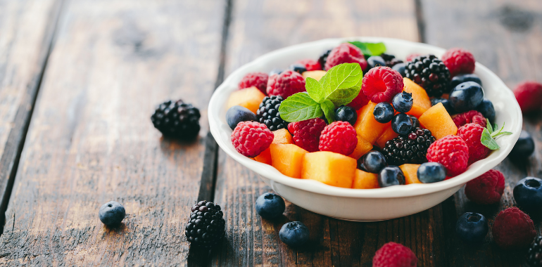 fruit berries grapes raspberries kiwi mango in white bowl on wood surface
